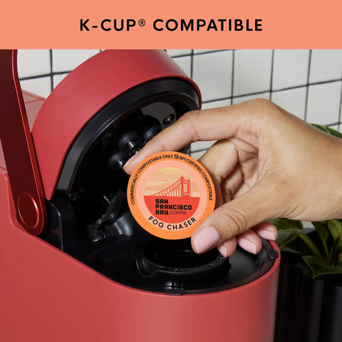 Person inserting Fog Chaser Medium Dark Roast K Cup Compatible Coffee Pods 80 Count Single Serve Compostable Pods into red coffee maker