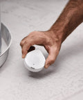 Hand placing Flo Smart Water Leak Detector For Home Protection Drip Or Flood Sensor Alarm With 24 7 Monitoring on the floor.