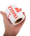 Hand holding a roll of Red Fragile Warning Stickers With Strong Adhesive For Handle With Care Labels On Shipping And Packing Boxes