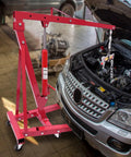 Heavy Duty Folding Hydraulic Engine Hoist And Crane, 2 Ton Capacity With Portable Wheels, red hoist beside open car hood.