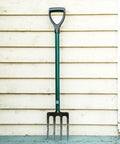 Compact Steel-Handle Border Fork With A 6-Inch Shorter Design For Tight Spots Built From 90 Percent Recycled High-Strength Steel Ergonomic Grip For All Day Comfort Lifetime Warranty No Bending Or Breaking Durable Yard Tool For Edges Beds And Borders against a wooden wall.