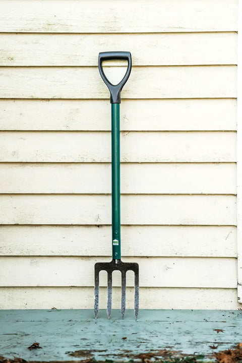 Compact Steel-Handle Border Fork With A 6-Inch Shorter Design For Tight Spots Built From 90 Percent Recycled High-Strength Steel Ergonomic Grip For All Day Comfort Lifetime Warranty No Bending Or Breaking Durable Yard Tool For Edges Beds And Borders against a wooden wall.