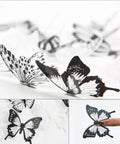 Close-up of 72 Piece Butterfly Wall Decor Sticker Set Removable 3D Mural Butterflies For Home Decor, Living Room And Kids Bedroom, Wall Decals For Parties, Birthdays, Weddings With Adhesive Dots, Black And White Vibe showing black and white butterflies with adhesive detail.