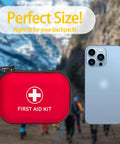 Red zippered first aid kit pouch with white cross; smartphone for scale in outdoor hiking scene.