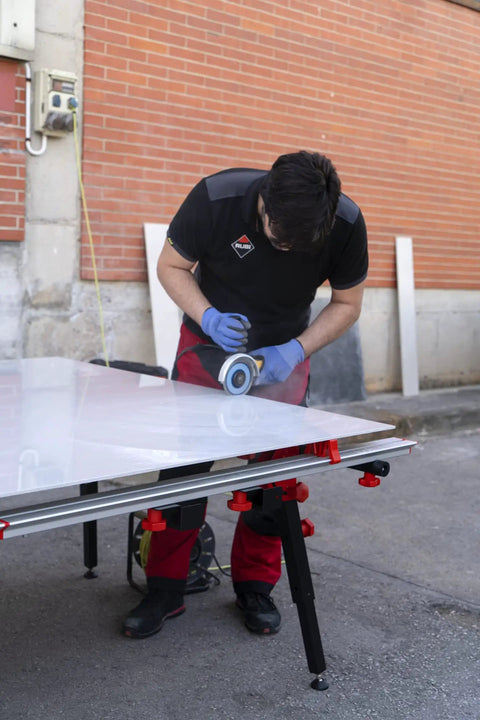 Man using a grinder on a heavy duty adjustable tile table for large format ceramic sheets, extending 43 to 59 inches.