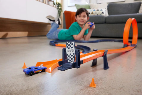 Child playing with Hot Wheels RC Speed Challenge Track Set with 1:64 scale car on a living room floor, showcasing loop and accessories.