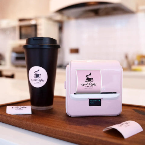 Kickass Portable Bluetooth Label Printer With Slick Wireless Tape Dispenser For Home Office Organization And Shipping Labels No Ink Required Mighty Handy Cordless Thermal Label Maker Handles Wide Continuous Rolls Daily on wooden tray with coffee cup.
