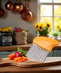 Orange-handled vegetable chopper with stainless steel crinkle blade on a cutting board with carrot slices