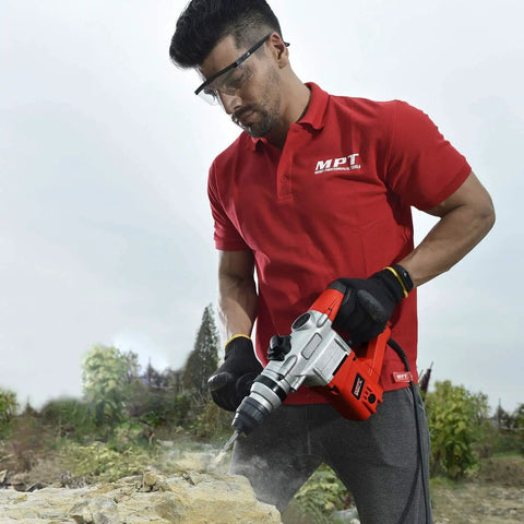 Man using Heavy Duty 1 Inch SDS Plus Rotary Hammer Drill With 8.5 Amp Power Three Modes Drill Hammer Chisel on rocky surface.