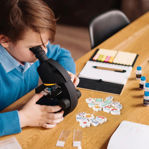 Boy using microscope with Science Mini Erasers 80 Pack With Eight Pattern Erasers Microscope U Shaped Magnets DNA on table.