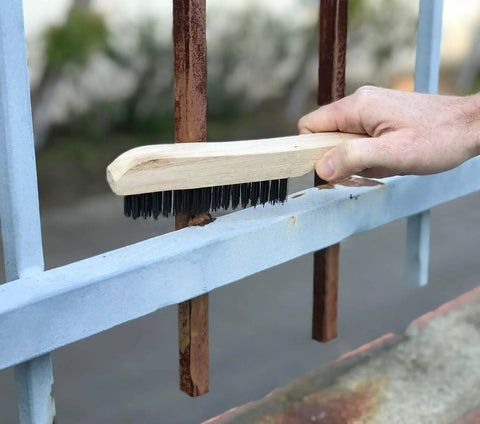 Using Four-Piece Shoe-Handle Wire Scratch Brush Set with black oil-tempered steel bristles on metal railing for rust removal.