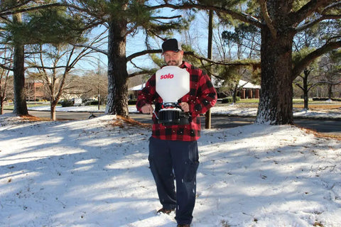 Man using 20 Pound Capacity Portable Chest Mount Spreader With Cross Shoulder Strap For Lawn Care And Garden Pros in snowy garden