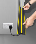 10 Ft Floor Cable Cover Protector Heavy Duty PVC Duct Easy To Unroll No Fuss Hide Cables At Home Office Or Outdoors No Trip Hazards Durable Cable Organizer For Wires being held open near wall socket.