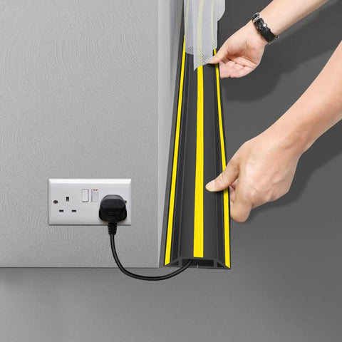 10 Ft Floor Cable Cover Protector Heavy Duty PVC Duct Easy To Unroll No Fuss Hide Cables At Home Office Or Outdoors No Trip Hazards Durable Cable Organizer For Wires being held open near wall socket.