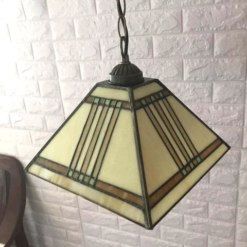 Mission Tiffany Style Stained Glass Ceiling Pendant Light With 11 Inch Lampshade And 47 Inch Tall Frame, lit against brick wall.