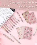 Floral Rose Pink Pen And Notepad Gift Set With 12 Flower Ballpoint Pens And 12 Pretty Notepads on a pink desk by a keyboard.