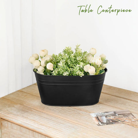 Black flower pot with artificial greenery and white flowers on wooden table, labeled 'Table Centerpiece'.