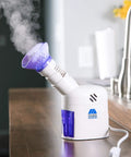 Home Spa Facial Steamer With Aromatherapy Diffuser And Soft Face Mask, emitting steam on a wooden counter in a kitchen setting.