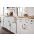 Modern kitchen with white cabinets and chrome hardware, featuring a farmhouse sink and a view of natural lighting.