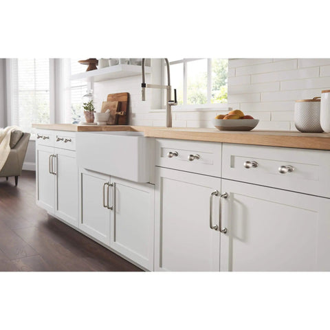 Modern kitchen with white cabinets and chrome hardware, featuring a farmhouse sink and a view of natural lighting.