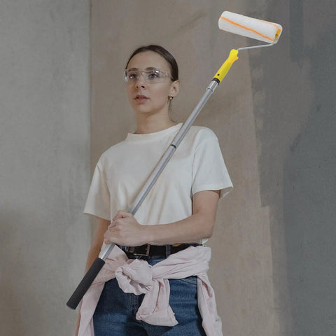 Kickass Detachable Microfiber Paint Roller Brush With Extended Telescopic Handle held by a woman wearing goggles and casual clothing.