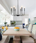 Rustic Matte Black 6 Light Candle Chandelier For Dining Room Kitchen Island Living Room And Foyer Industrial 26 Inch Ceiling Light Fixture Modern Farmhouse Style Black Chandeliers over dining table with windows in background.