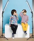 Children sit between the 180 LED Photography Studio Lighting Kit With Pro Grade Handheld Wand Light On Stand And Tripod Plus Bag For Photo And Video Filming