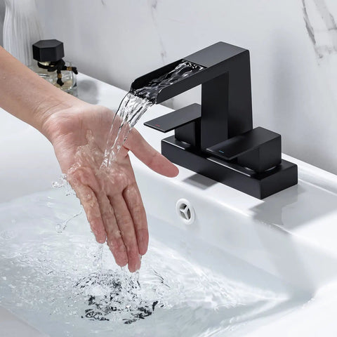 4 Inch Centerset Vanity Sink Faucet With Dual Handle Waterfall Spout Three Hole Basin Mixer Dope Matte Black Finish With Overflow Pop Up Drain Easy Install Bathroom Tap For Modern Bathrooms with water flowing over hand.