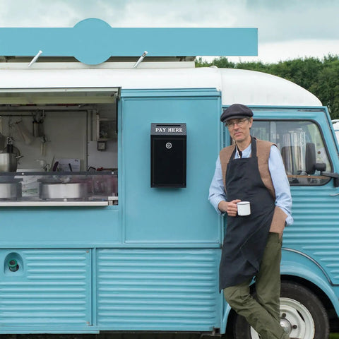 Man in apron next to food truck with Locking Cash Box With Slot For Donations, Metal Money Box, wall-mounted on blue vehicle.