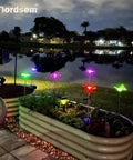 Solar Garden Lights Outdoor Set Of 6 Insect Stake Lights illuminating planters by a lake at night with colorful LED beams.