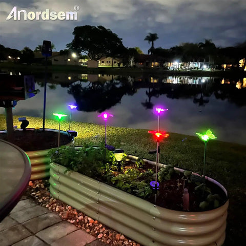 Solar Garden Lights Outdoor Set Of 6 Insect Stake Lights illuminating planters by a lake at night with colorful LED beams.