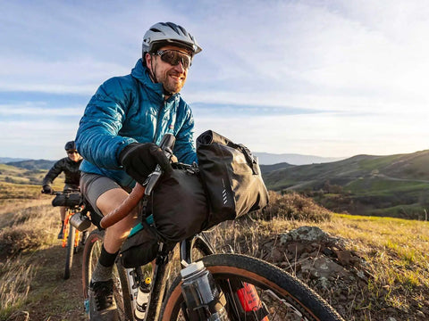Cyclist using Front Loader 8L Waterproof Handlebar Bike Bag for Bikepacking With Removable Dry Bag Quick Release Mounts