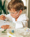 Child using Science Mini Erasers 80 Pack with Eight Pattern Erasers, wearing goggles, writing in a notebook at a desk.