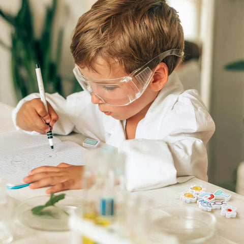 Child using Science Mini Erasers 80 Pack with Eight Pattern Erasers, wearing goggles, writing in a notebook at a desk.