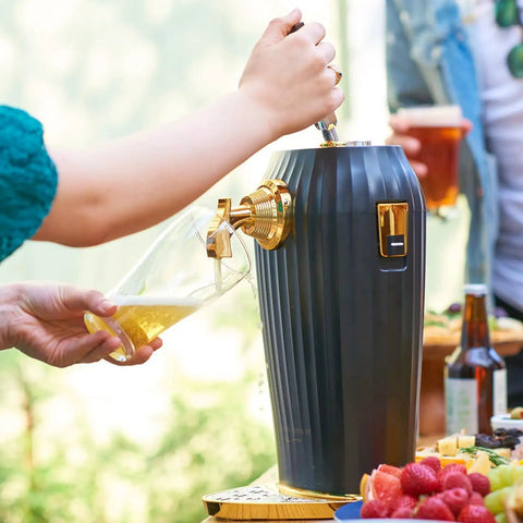 Person pouring beer from Portable Electric Ultrasonic Foam Maker Craft Beer And Cocktail Dispenser into a glass outdoors.