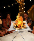 22 Inch Outdoor Folding Fire Pit For Camping And Backyard Fun with friends gathered around, lit on fire, made of 304 stainless steel.