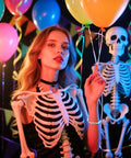 Woman in skeleton costume holding balloons with skull decoration, festive party setup with colorful lights and Halloween theme