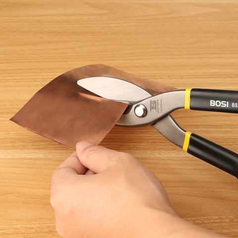 Close-up of BOSI tin snips 12-inch, flat blade cutting copper sheet on wood bench