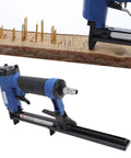 Heavy Duty Pneumatic Brad Nailer And Air Stapler Featuring Split Body And Heat Treated Nozzle for woodworking on a wood plank.