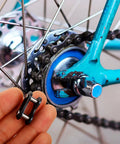 Hand holding a black connector link for a bicycle chain near the rear wheel, showcasing 10 Pack Bicycle Chain Link Connector Single Speed Wheel Beefy Roller Steel No Drama Quick Fix Kit Adult And Youth Cycling Rig Engineered For Easy Install And Smooth Road Cruising Vibes.