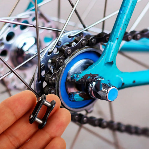 Hand holding a black connector link for a bicycle chain near the rear wheel, showcasing 10 Pack Bicycle Chain Link Connector Single Speed Wheel Beefy Roller Steel No Drama Quick Fix Kit Adult And Youth Cycling Rig Engineered For Easy Install And Smooth Road Cruising Vibes.