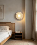MECOLA Round Resin Accent Wall Sconce Small Glass Globe Shade Wall Lamp illuminating a cozy bedroom with concentric ripple design.