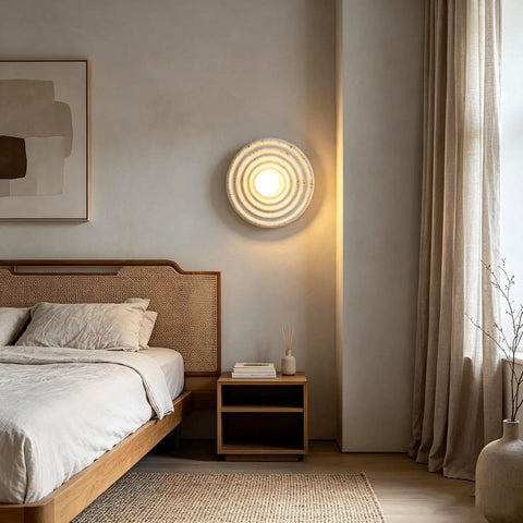 MECOLA Round Resin Accent Wall Sconce Small Glass Globe Shade Wall Lamp illuminating a cozy bedroom with concentric ripple design.