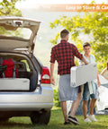 Two people carrying a folded 4 Ft Folding Camping Picnic Table Set With Seats And Umbrella Hole, Grab-And-Go Suitcase-Style Lightweight Aluminum Alloy Frame Table For RVs near a car.