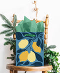 Gift bag with lemon design, tissue paper handles on a wooden chair, part of the Clash Flowers Gift Bags With Tissue Paper Handles Pack Of 6 Medium Size Recyclable Cardboard Gift Bags For Party Favor Or Gift Wrapping Dope Floral Pattern And Eco Friendly Packaging.