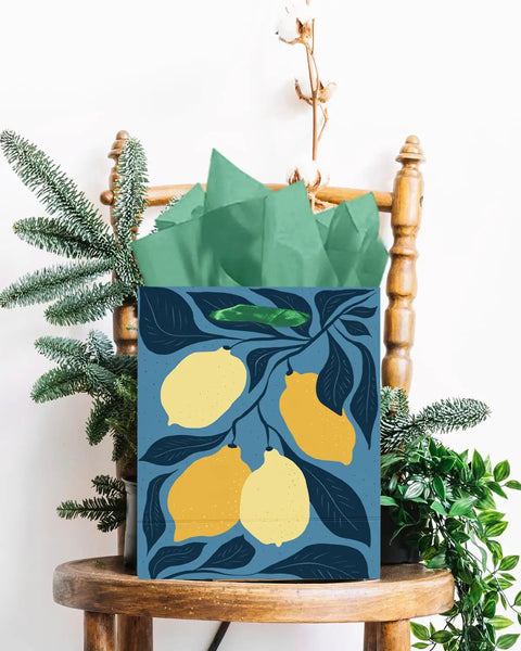 Gift bag with lemon design, tissue paper handles on a wooden chair, part of the Clash Flowers Gift Bags With Tissue Paper Handles Pack Of 6 Medium Size Recyclable Cardboard Gift Bags For Party Favor Or Gift Wrapping Dope Floral Pattern And Eco Friendly Packaging.