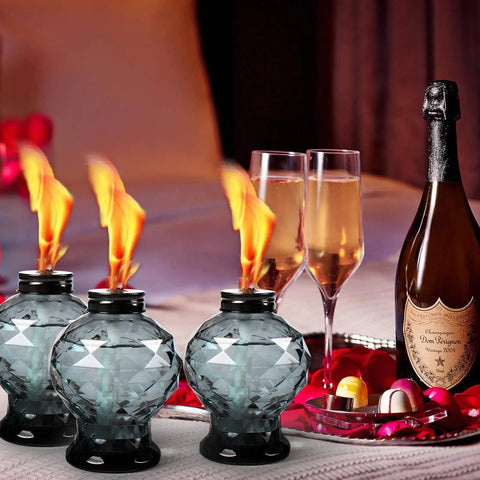 Four Pack Glass Table Torches With Citronella For Outdoor Patio And Garden, Crystal Gem Design, lit beside champagne glasses.