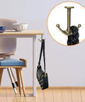 Zinc Alloy Double Prong Ceiling Hooks 4 Pack Bronze Finish for Towels Coats Hats Robes and More Under Shelf Kitchen Bathroom Cabinet Garage Use Durable Rust Resistant Hardware mounted on table edge holding a bag.