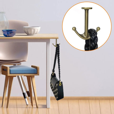 Zinc Alloy Double Prong Ceiling Hooks 4 Pack Bronze Finish for Towels Coats Hats Robes and More Under Shelf Kitchen Bathroom Cabinet Garage Use Durable Rust Resistant Hardware mounted on table edge holding a bag.