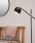 60-Inch Floor Lamp With Matte Black Finish, Brass Pivot, Metal Shade, Inline On Off Foot Switch beside a wooden bed in a bedroom.